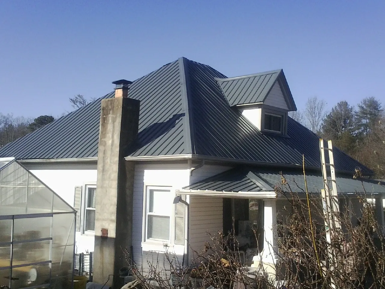 Dark blue standing seam metal roof on a white farmhouse with dormer — Slate & Tile Roof Repair by Roofing Brothers in Briarcliff Manor
