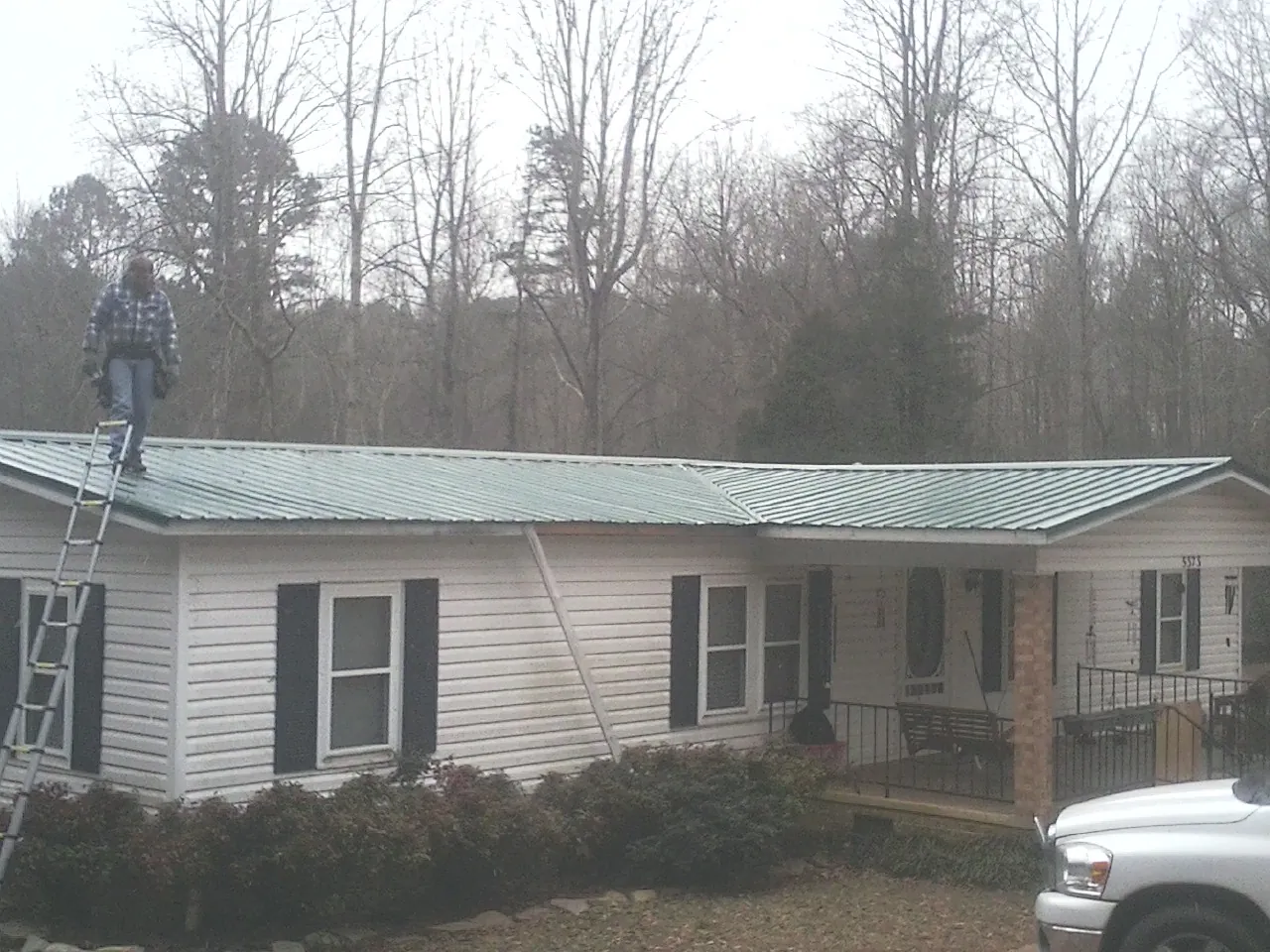 Worker on a ladder beside a new green metal roof on a ranch home in Briarcliff Manor