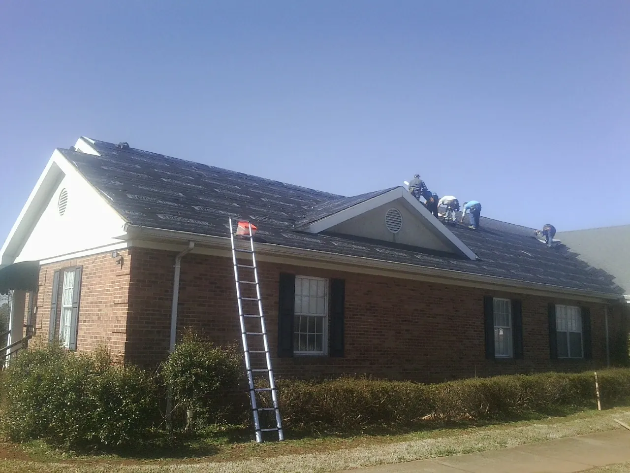 Crew tearing shingles off a brick ranch roof with a ladder set — Emergency Roof Repair work by our crew in Briarcliff Manor
