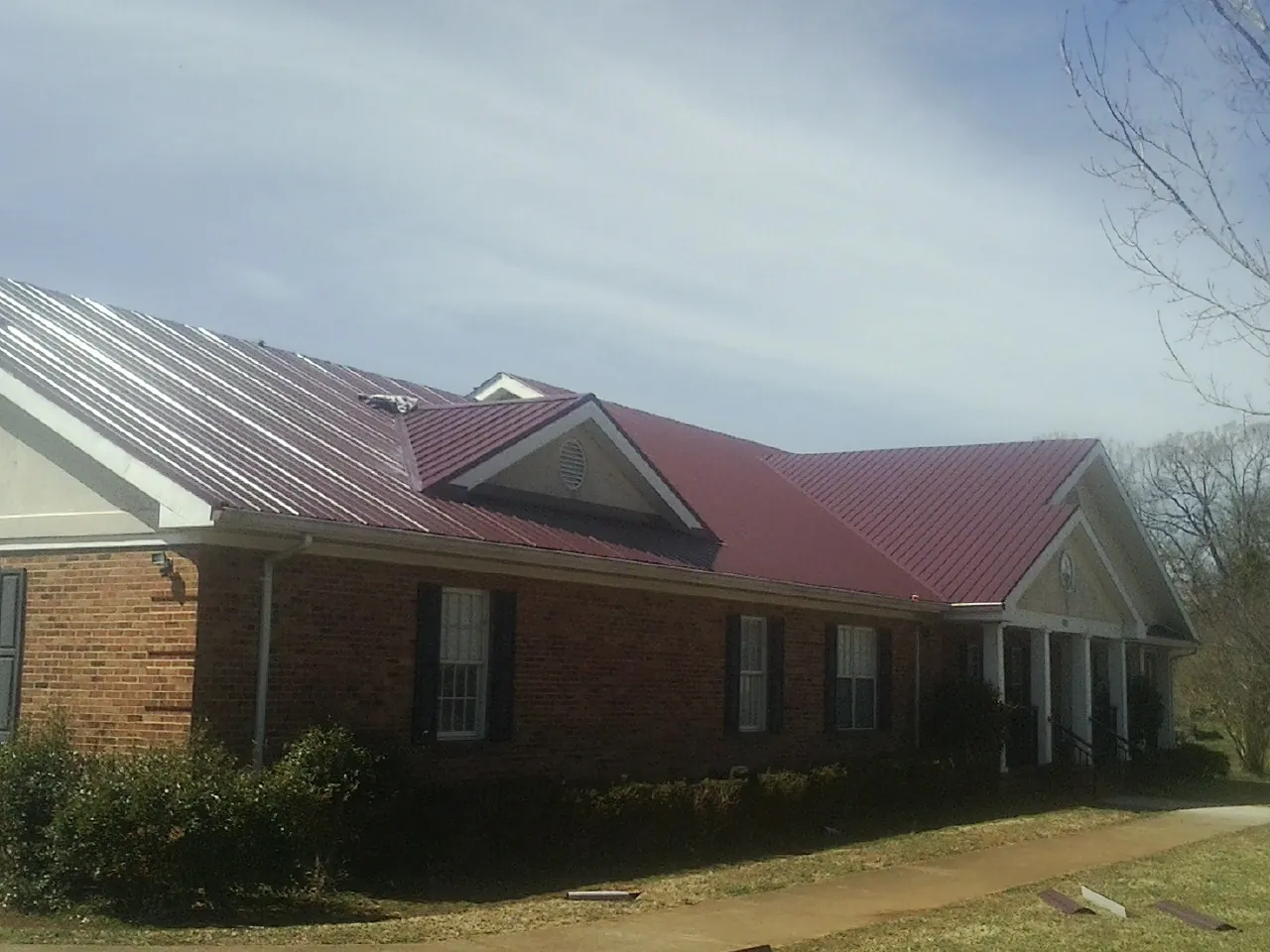 Red metal roof with gabled entries on a long brick building, from a Hail Damage Roof Repair job in Briarcliff Manor