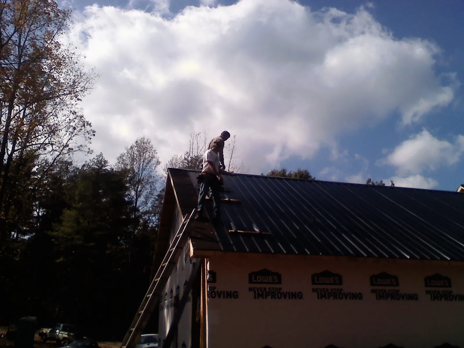 Roofer fastening dark metal panels high against a cloudy sky, from a Roof Inspection job in Briarcliff Manor