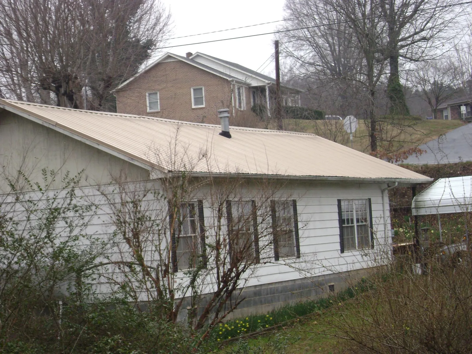 Tan metal roof on a white sided house set into a hillside — Commercial Roofing by Roofing Brothers in Briarcliff Manor